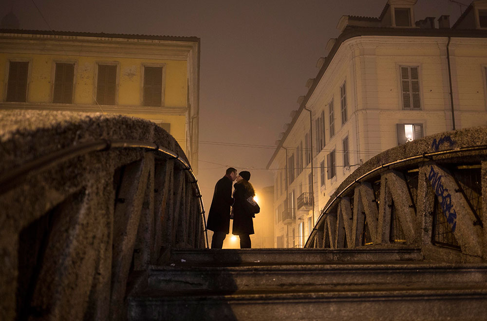 Momento romántico. Una pareja se da un beso sobre un puente que cruza el canal Naviglio Grande, durante una neblinosa tarde en Milán, Italia.