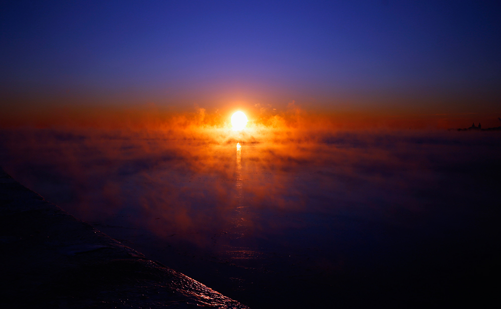 Del crepúsculo al amanecer. El sol comienza a salir sobre el lago Michigan, en medio de la bruma invernal, en la ciudad de Chicago, Estados Unidos.